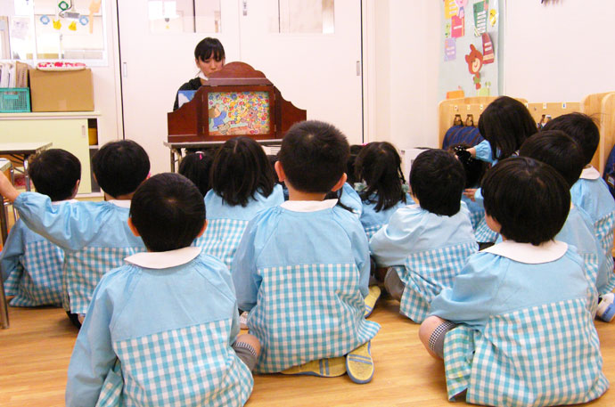 先生が子どもに紙芝居を読み聞かせている様子